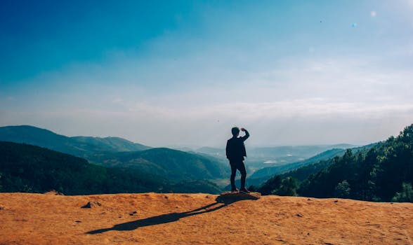 pexels-photo-1087735-1087735 A lone traveler stands on a hilltop, gazing over a vast mountain landscape under a clear blue sky.